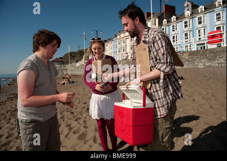 zwei unternehmungslustige junge Studenten, kalte Getränke und Eis am Stiehl an Menschen am Strand von Aberystwyth, auf einen heißen Sommer Nachmittag UK zu verkaufen Stockfoto