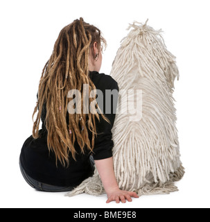 Rückansicht des geschnürten weißen Pudel und ein Mädchen mit Dreadlocks sitzen vor weißem Hintergrund Stockfoto