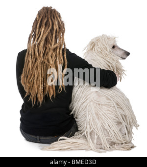 Rückansicht des geschnürten weißen Pudel und ein Mädchen mit Dreadlocks sitzen vor weißem Hintergrund Stockfoto