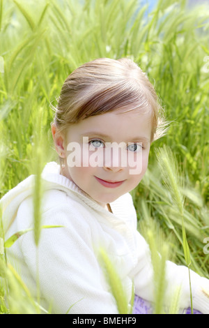 glückliches lächelndes blondes Mädchen sitzen auf grünen Spitzen Wiese Stockfoto