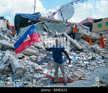 Ein Mann Wellen der haitianischen Flagge in Port au Prince & Such-und Rettungsteams suchen den Trümmern nach Überlebenden des Erdbebens in Haiti Stockfoto