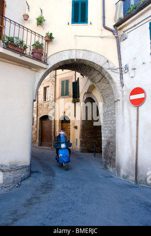 Mann reitet einen blaue Vespa Motorroller durch ein altes Tor in Spello, Provinz Perugia, Umbrien, Italien Stockfoto