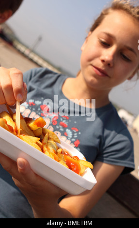 Teenager-Mädchen einen Teil der Späne aus einem Plastikbehälter mit hölzernen Form im Freien zu essen Stockfoto