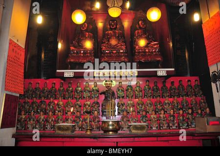 3 rote Buddhas sitzen oben Gottheit Figurinen, Räucherstäbchen und Weihrauch-Brenner, Pak Sing Ancestral Hall, Sheung Wan, Hong Kong Stockfoto