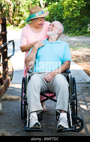 Ältere Mann im Rollstuhl deaktiviert mit seiner liebevollen Frau kümmert sich um ihn. Stockfoto