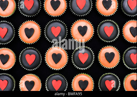 Mini-Muffins mit schwarz und orange Vereisung und Herz Formen verziert Stockfoto