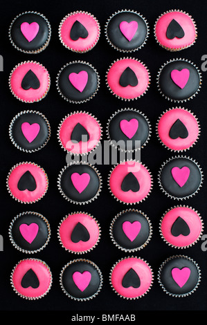 Mini-Muffins mit schwarz und rosa Zuckerguss und Herz Formen verziert Stockfoto