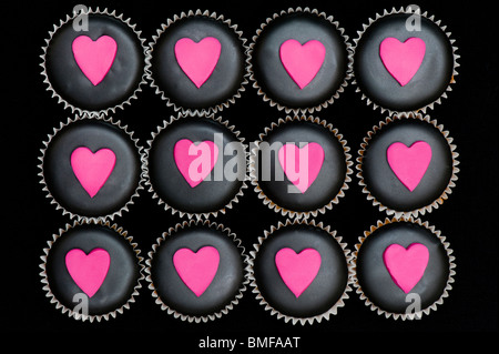 Mini-Muffins mit schwarz und rosa Zuckerguss und Herz Formen verziert Stockfoto