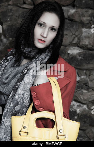 junge Frau mit gelben Handtasche posiert in roten Mantel Stockfoto