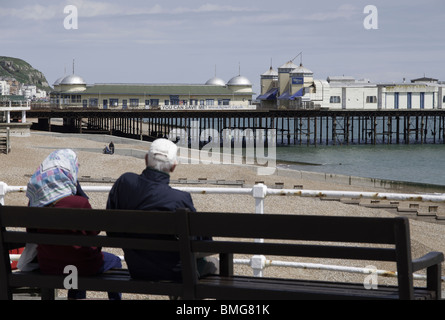 Ein paar Pause neben dem Meer bei Hastings, East Sussex und Blick auf den pier Stockfoto