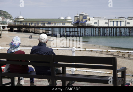 Ein paar Pause neben dem Meer bei Hastings, East Sussex und Blick auf den pier Stockfoto