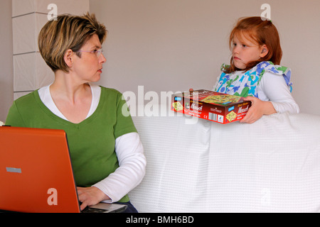 eine Mutter, die versucht, auf ihrem Computer zu arbeiten, während ihre Tochter mit ihr spielen will Stockfoto