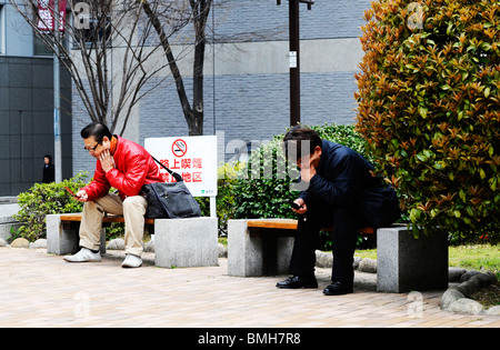 Zwei Männer sitzen auf dem Handy durch die Blumenuhr in Kobe Japan sprechen Stockfoto