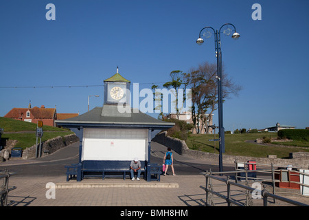 ein Mann sitzt auf Promenade Pavillion mit Uhr von der Anlegestelle / Pier im morgendlichen Sonnenlicht bei Swanage Stockfoto