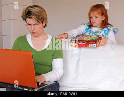 eine Mutter, die versucht, auf ihrem Computer zu arbeiten, während ihre Tochter mit ihr spielen will Stockfoto