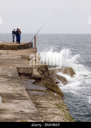 Drei Männer Makrelen angeln am Ende des South Gare Wellenbrechers an Teesport mit einer brechenden Welle. Stockfoto