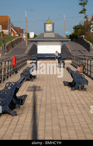 ein Mann sitzt auf Promenade Pavillion mit Uhr von der Anlegestelle / Pier im morgendlichen Sonnenlicht bei Swanage Stockfoto