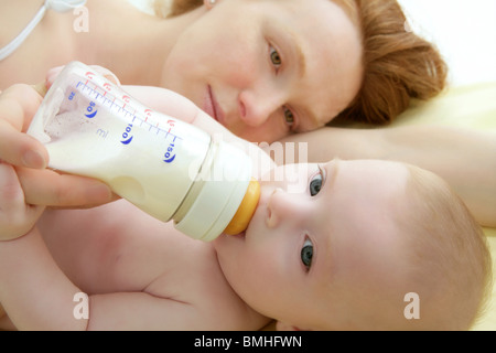 Baby Blond Trinkflasche aus Mutter Händen Stockfoto