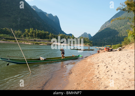 Ein Lao Mann schiebt aus in seinem Kanu vom Ufer des Flusses am Fluss Nam Ou in Nordlaos mit Bergen im Hintergrund Stockfoto