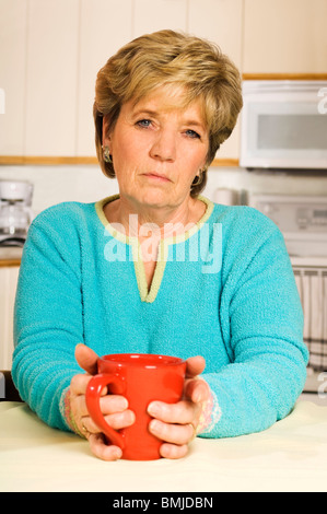 Ältere Frau hält eine Kaffeetasse suchen unglücklich. Stockfoto