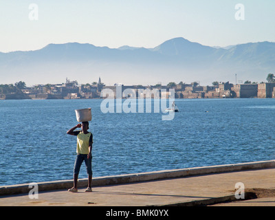 Eine Frau trägt einen Eimer entlang der Strandpromenade in Cap Haitien, Haiti Stockfoto