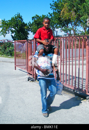 Ein Mann trägt seinen verletzten Sohn und einen Beutel mit Essen heraus in Port-au-Prince nach dem Erdbeben in Haiti Stockfoto
