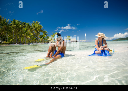 Ein Mann und eine Frau an einem Strand eine tahitian Hotelanlage mit Schnorchelausrüstung (Flossen und Maske). Sie sind auf Sand Sonnenbaden. Stockfoto