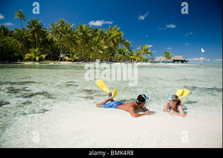 Ein Mann und eine Frau an einem Strand eine tahitian Hotelanlage mit Schnorchelausrüstung (Flossen und Maske). Sie sind auf Sand Sonnenbaden. Stockfoto