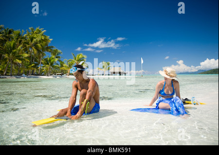 Ein Mann und eine Frau an einem Strand eine tahitian Hotelanlage mit Schnorchelausrüstung (Flossen und Maske). Sie sind auf Sand Sonnenbaden. Stockfoto