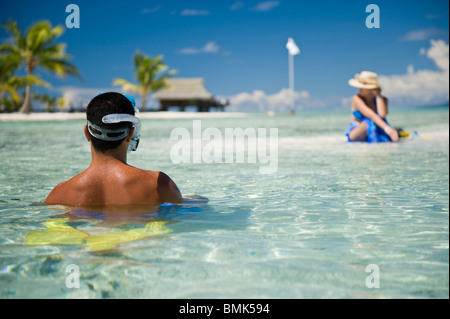 Ein Mann und eine Frau an einem Strand eine tahitian Hotelanlage mit Schnorchelausrüstung (Flossen und Maske). Sie sind auf Sand Sonnenbaden. Stockfoto