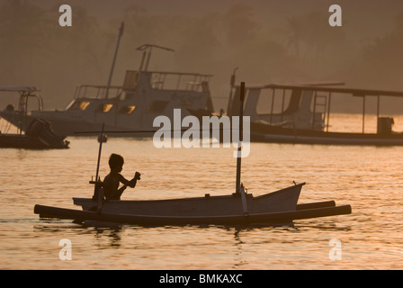 Ein balinesischer junge Paddel bei Sonnenaufgang in einer traditionellen Fischfang Ausleger genannt Jukung im Dorf Pemuteran. Stockfoto