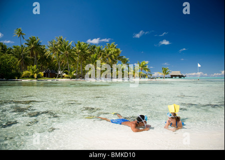 Ein Mann und eine Frau an einem Strand eine tahitian Hotelanlage mit Schnorchelausrüstung (Flossen und Maske). Sie sind auf Sand Sonnenbaden. Stockfoto