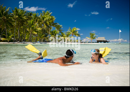 Ein Mann und eine Frau an einem Strand eine tahitian Hotelanlage mit Schnorchelausrüstung (Flossen und Maske). Sie sind auf Sand Sonnenbaden. Stockfoto