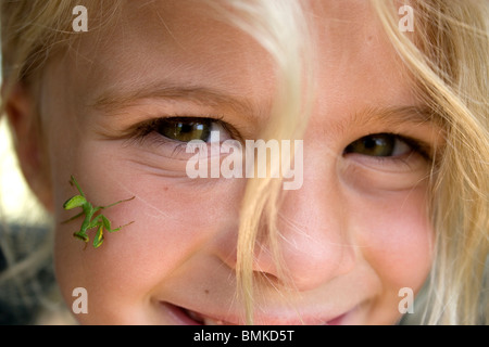 Afrika, Kenia. Gottesanbeterin auf junge Mädchen Gesicht. Stockfoto