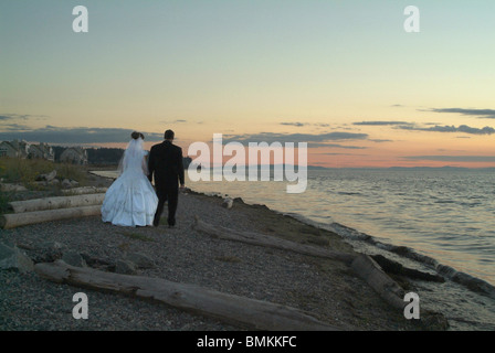 Braut und Bräutigam zu Fuß entlang der Küste in der Abenddämmerung Stockfoto