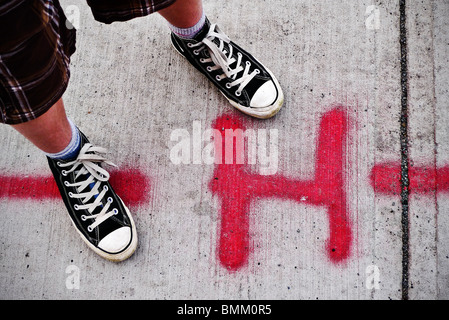 Städtischen Jugend mit Converse Chino neben spray lackiert H auf Bürgersteig. Stockfoto