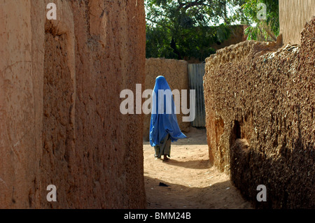 Niamey, Niger Frau trägt einen langen blauen Tchador zu Fuß in den Straßen von einem Schlamm-Häuser-Dorf Stockfoto