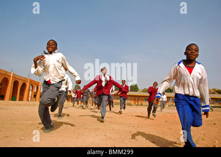 Nigeria, Jos, Schüler und Schülerinnen in ihren lila und blau Schuluniform laufen insgesamt auf einem sandigen Feld. Stockfoto