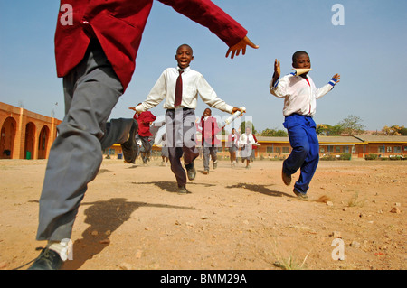 Nigeria, Jos, Schüler und Schülerinnen in ihren lila und blau Schuluniform laufen insgesamt auf einem sandigen Feld. Stockfoto