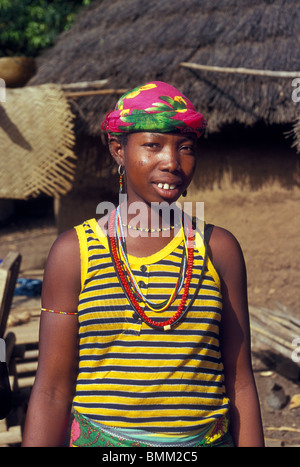 Eine Frau in einem gelben abgespeckte Tank-Top T-shirt posiert vor ihrem Lehmhaus in abgelegenen Bedik Dorf von Iwol in Senegal, Stockfoto