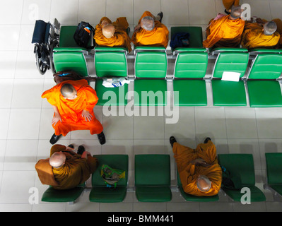 Eine Gruppe orangefarbener Thai-Mönche, die auf grünen Bänken sitzen, warten auf ihren Flug nach Zürich Kloten (ZRH/LSZH), Bangkok TH Stockfoto