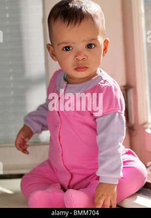 Niedliche sieben Monate altes Baby Mädchen sitzen auf einem Fensterbrett Stockfoto