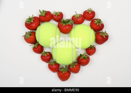 Lebhafte rote Erdbeeren in der Form eines Herzens Liebe vor einem weißen Hintergrund mit Tennisbällen im Zentrum Stockfoto