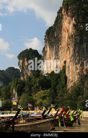 vertikales Bild des long-Tail-Boote auf West Railay Beach, Thailand, mit Klippe hinter Stockfoto