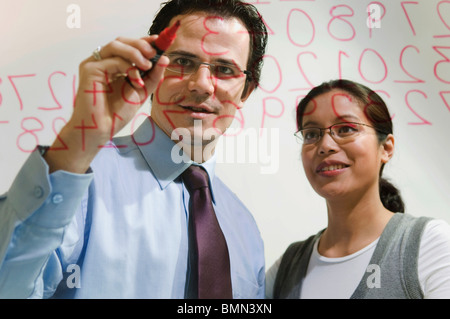 Mann und Frau arbeiten auf Zahlen auf Glas Stockfoto