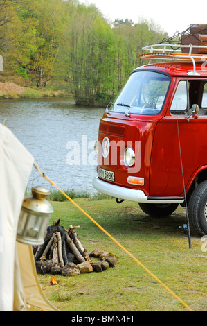 Ein leuchtend roter VW-Wohnmobil mit Dachgepäckträger, der vor einem Glockenzelt an einem See abgestellt ist. Stockfoto