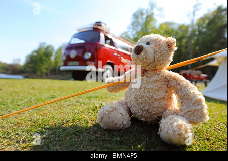 Ein Teddybär genießt einen Campingurlaub in einem leuchtend roten klassischen VW-Wohnmobil. Stockfoto