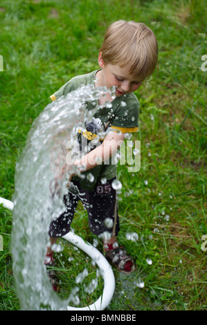 Ein junges Kind junge Wasser Garten Rasen und Blumen mit Wasser aus einem Schlauch Stockfoto