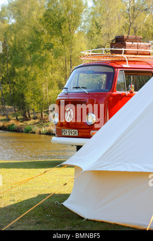 Ein leuchtend roter VW-Wohnmobil mit Dachgepäckträger, der vor einem Glockenzelt an einem See abgestellt ist. Stockfoto