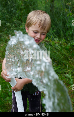 Ein junges Kind junge Wasser Garten Rasen und Blumen mit Wasser aus einem Schlauch Stockfoto